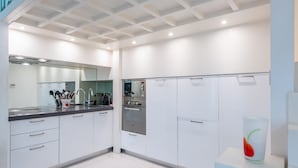Une cuisine moderne avec des meubles blancs, des appareils en acier inoxydable et un vase en verre contenant une fleur rouge.