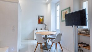 Un espace repas moderne avec une table ronde et quatre chaises, un téléviseur à écran plat fixé au mur et une fenêtre laissant entrer la lumière naturelle.