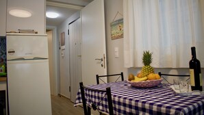 A compact kitchen with a refrigerator, a dining table with a checkered tablecloth, and a fruit bowl. - Alkyon Perea Apartments (Thermaikos)
