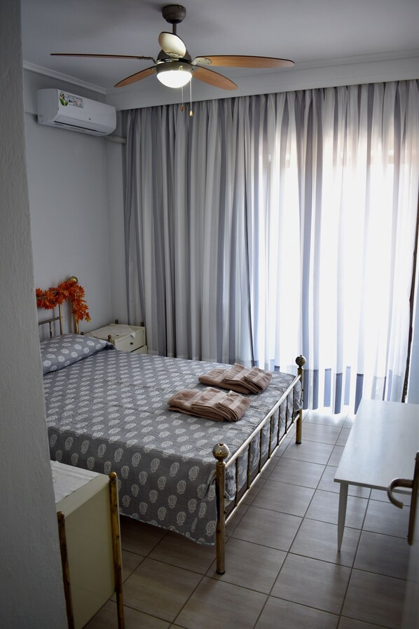 A bedroom with a bed, a desk, a chair, a ceiling fan, and a window with curtains.