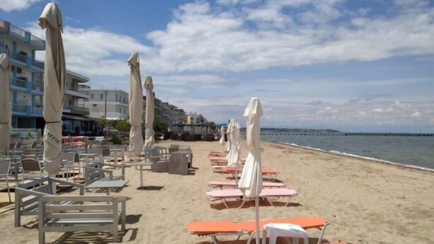 A beach with rows of sun loungers and umbrellas, a clear sky, and buildings in the background. - Alkyon Perea Apartments (Thermaikos)