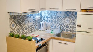 A compact kitchen with white cabinets, a built-in oven, a sink, and patterned backsplash tiles. - Alkyon Perea Apartments (Thermaikos)
