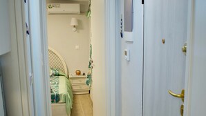 A narrow hallway leading to a bedroom with a bed, a nightstand, and a wall-mounted air conditioner. - Alkyon Perea Apartments (Thermaikos)