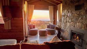 A cozy log cabin interior with a stone fireplace, plush seating, and a scenic view.