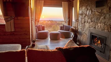 L’intérieur chaleureux d’un chalet en bois avec une cheminée en pierre, des fauteuils confortables et une vue magnifique.
