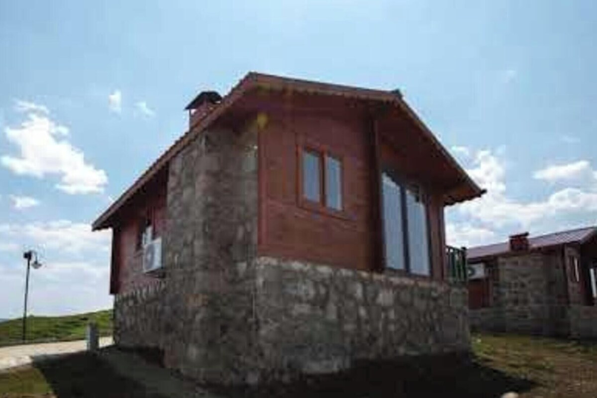 A small, single-story building with a stone foundation and a red roof, situated on a grassy area with a clear sky.