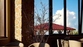 Interior de restaurante con paredes de piedra, ventanas amplias y plantas de interior.