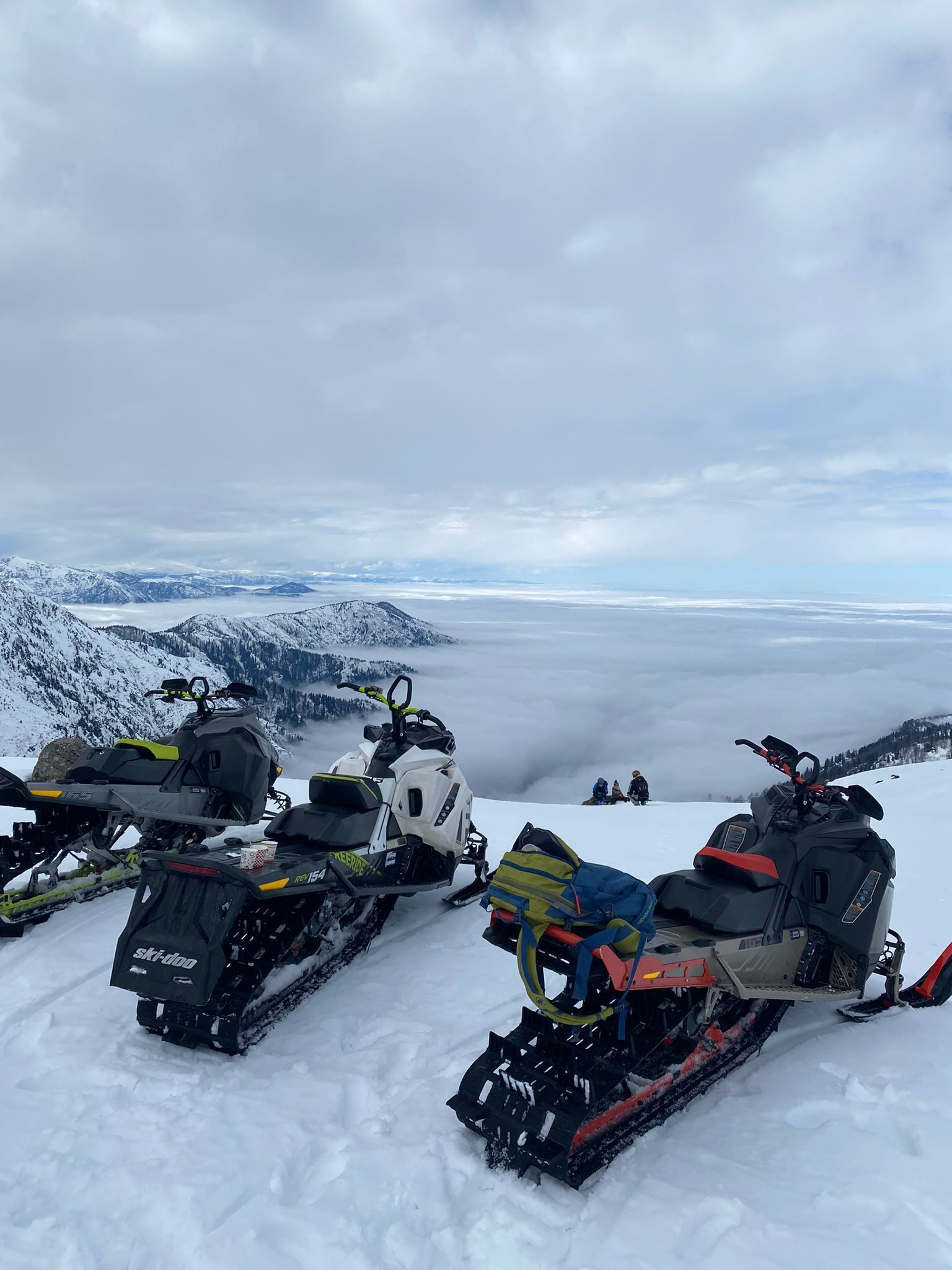 Motos de nieve estacionadas en una montaña nevada con vista a un valle y montañas distantes.