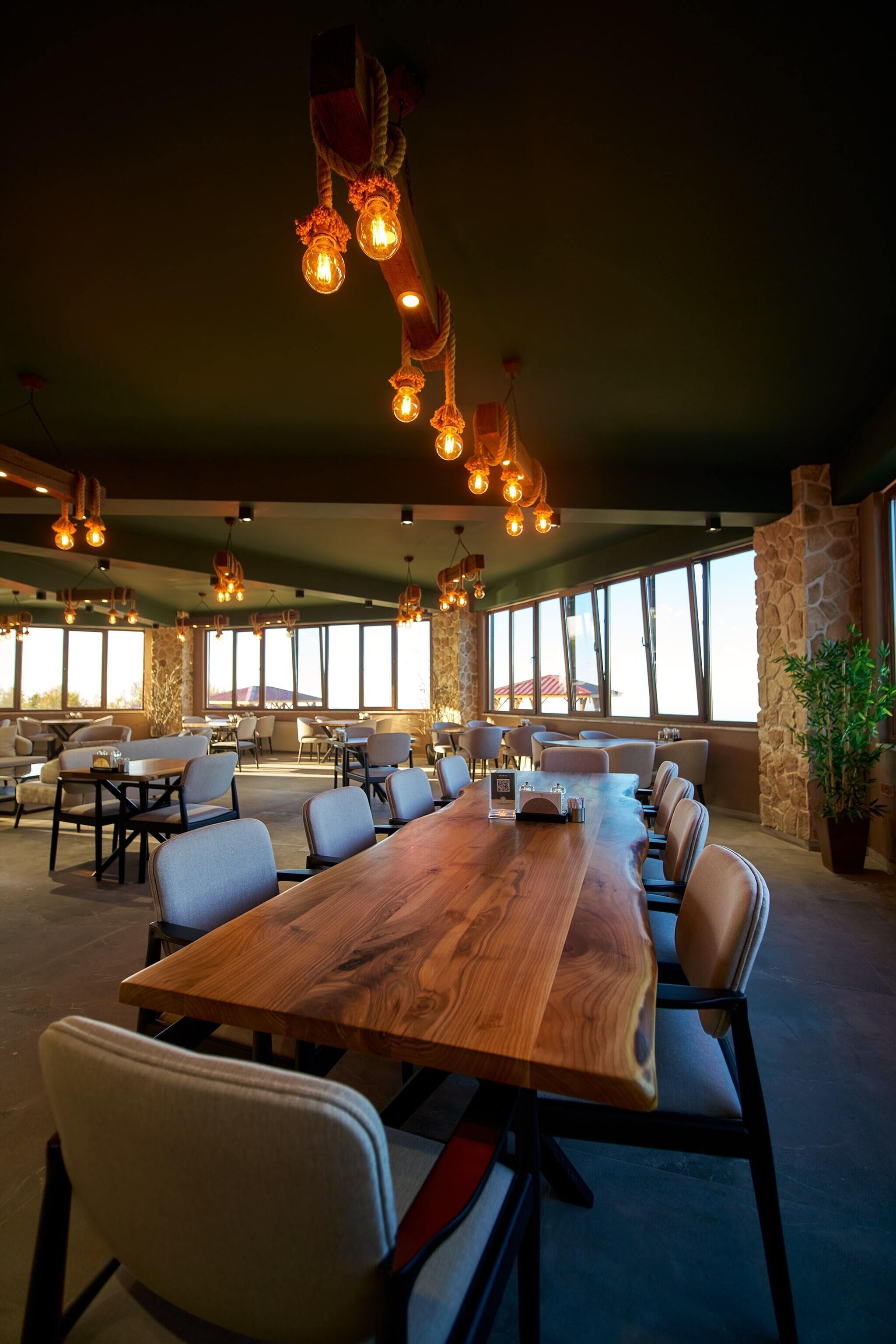 Uma sala de conferências ampla, com uma longa mesa de madeira, várias cadeiras e luminárias pendentes.