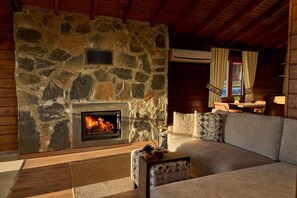 A stone fireplace with a fire, a sofa, and a small table with a plant. - Flora Handüzü Resort & Wellness Bungalow Hotel (Güneysu)