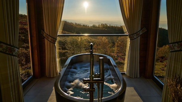 A hot tub with a view of a forested landscape through a large window.