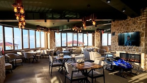 A spacious indoor area with multiple tables and chairs, a stone wall, a fireplace, and a mounted television.