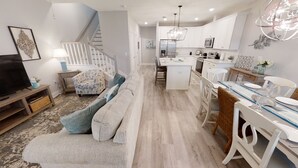 Una cocina moderna con armarios blancos, una isla central y un comedor con mesa y sillas blancas.