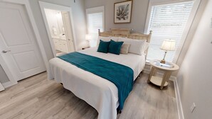 Un dormitorio con cama, mesita de noche, lámpara, espejo y ventana con persianas.