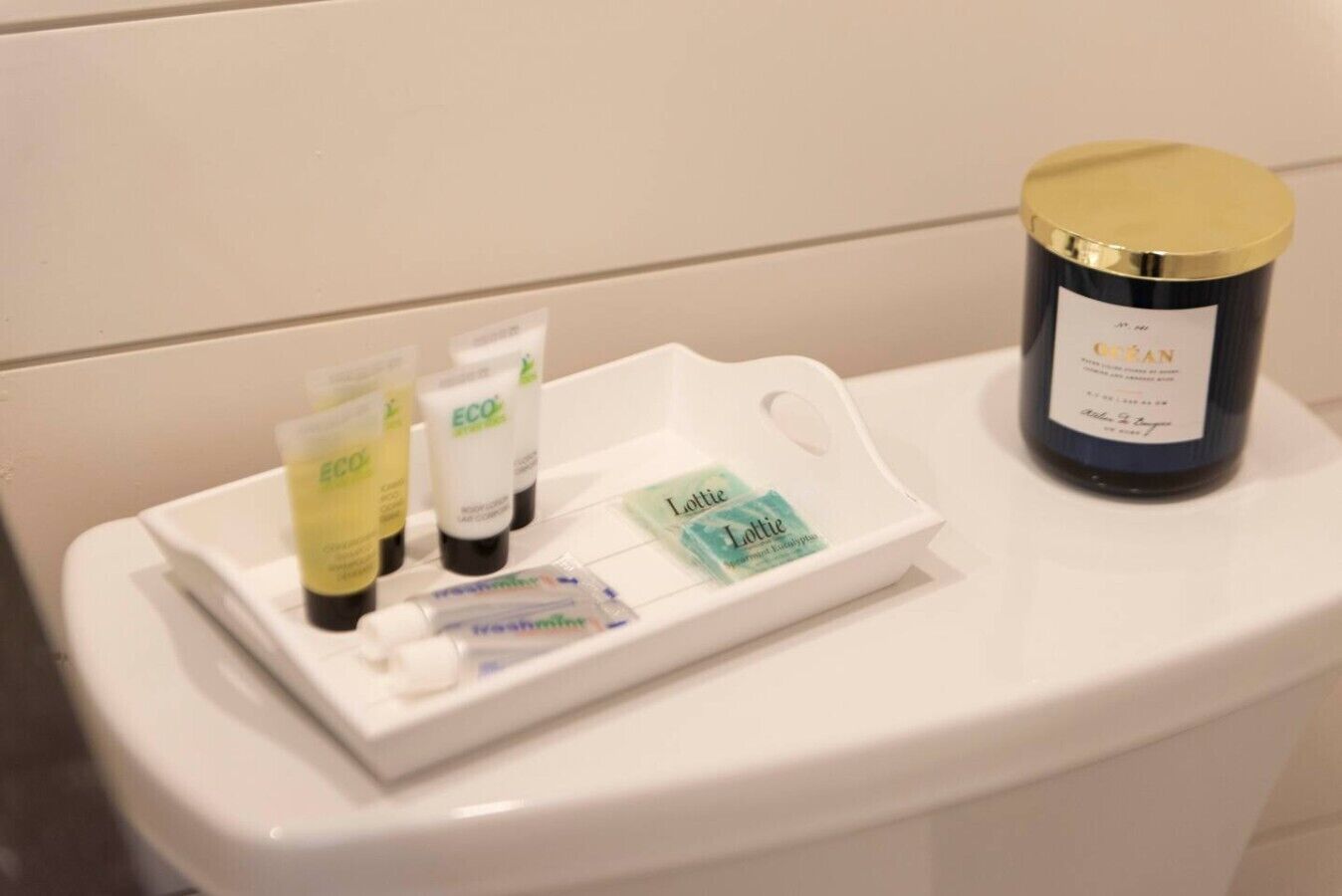 Toiletartikelen op een witte schaal naast een blauwe kaars op een witte toilet.