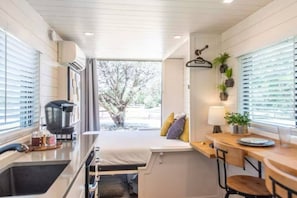 A compact kitchenette with a coffee maker, a small sink, and a window with blinds.