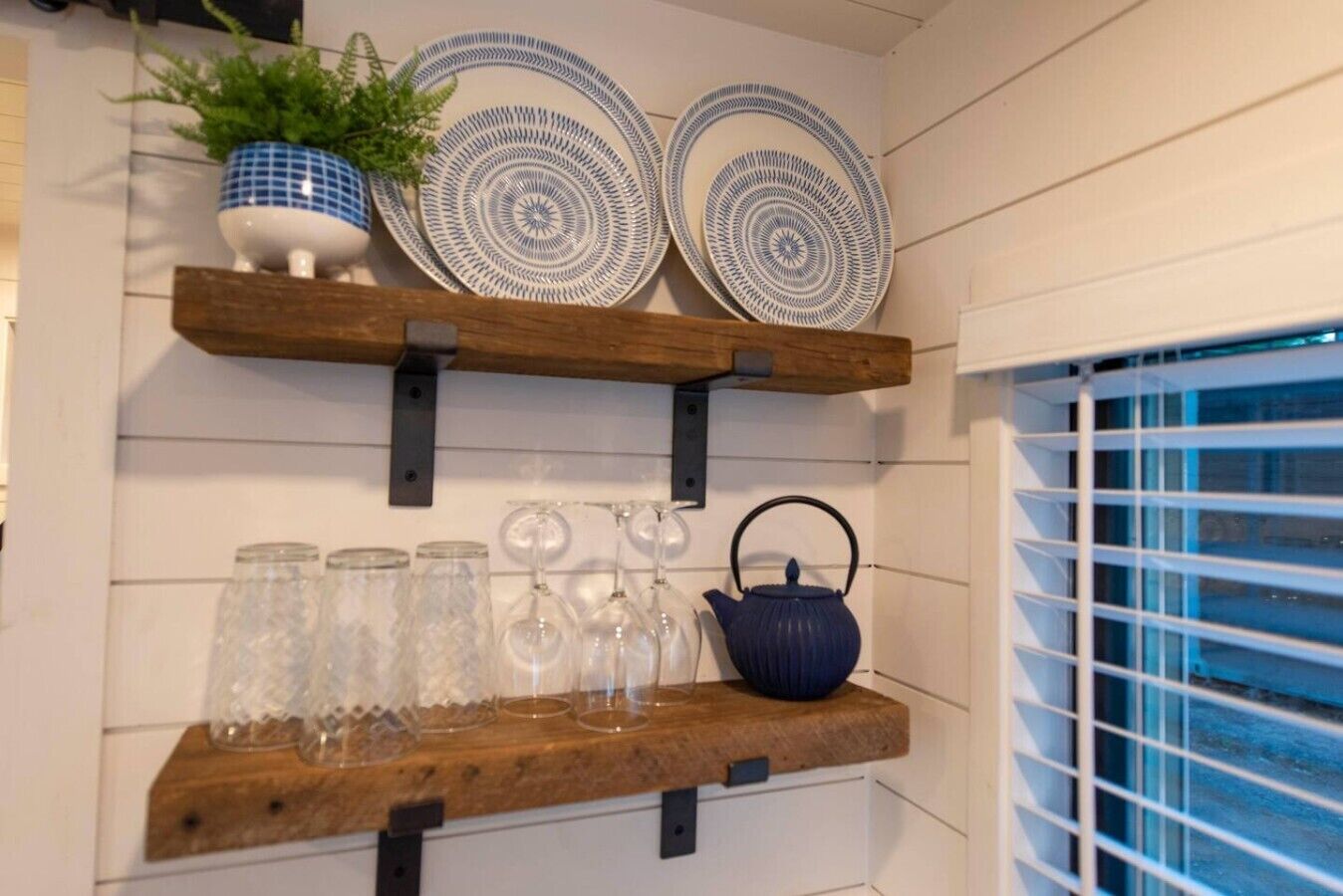 Una repisa de cocina con platos decorativos, una planta en maceta y cristalería.