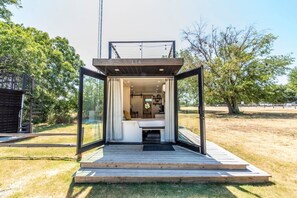 A modern, open-plan interior with a bed, seating area, and a view of the outdoors. - Honeycomb Container Home | "Pickleball Court!" (Waco)