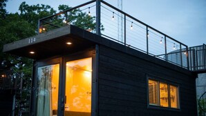 A modern building with a balcony, a visible room with a window, and a number '114' on the facade. - Honeycomb Container Home | "Pickleball Court!" (Waco)
