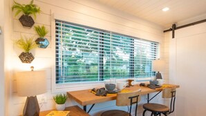 A kitchen with a large window, bar stools, and a countertop with a plant and a book. - Honeycomb Container Home | "Pickleball Court!" (Waco)