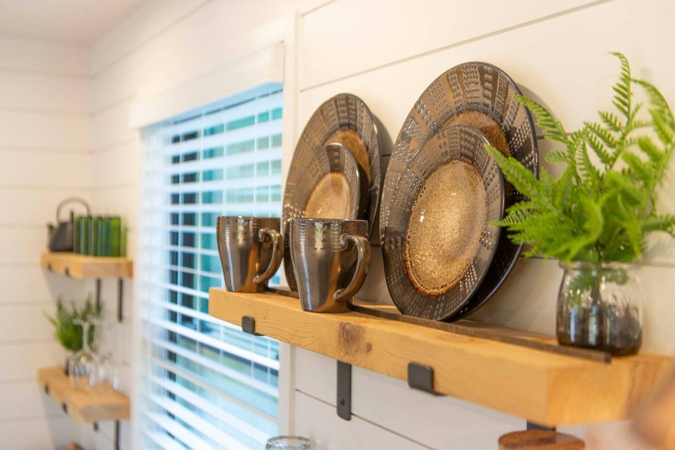 Une étagère de cuisine contenant divers ustensiles de métal, notamment des assiettes et des tasses, ainsi qu’une plante en pot.
