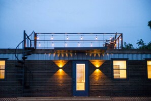 A building with a wooden facade, a blue door, and multiple windows. - "The Woods" Container | Pickleball | Rooftop Patio (Waco)