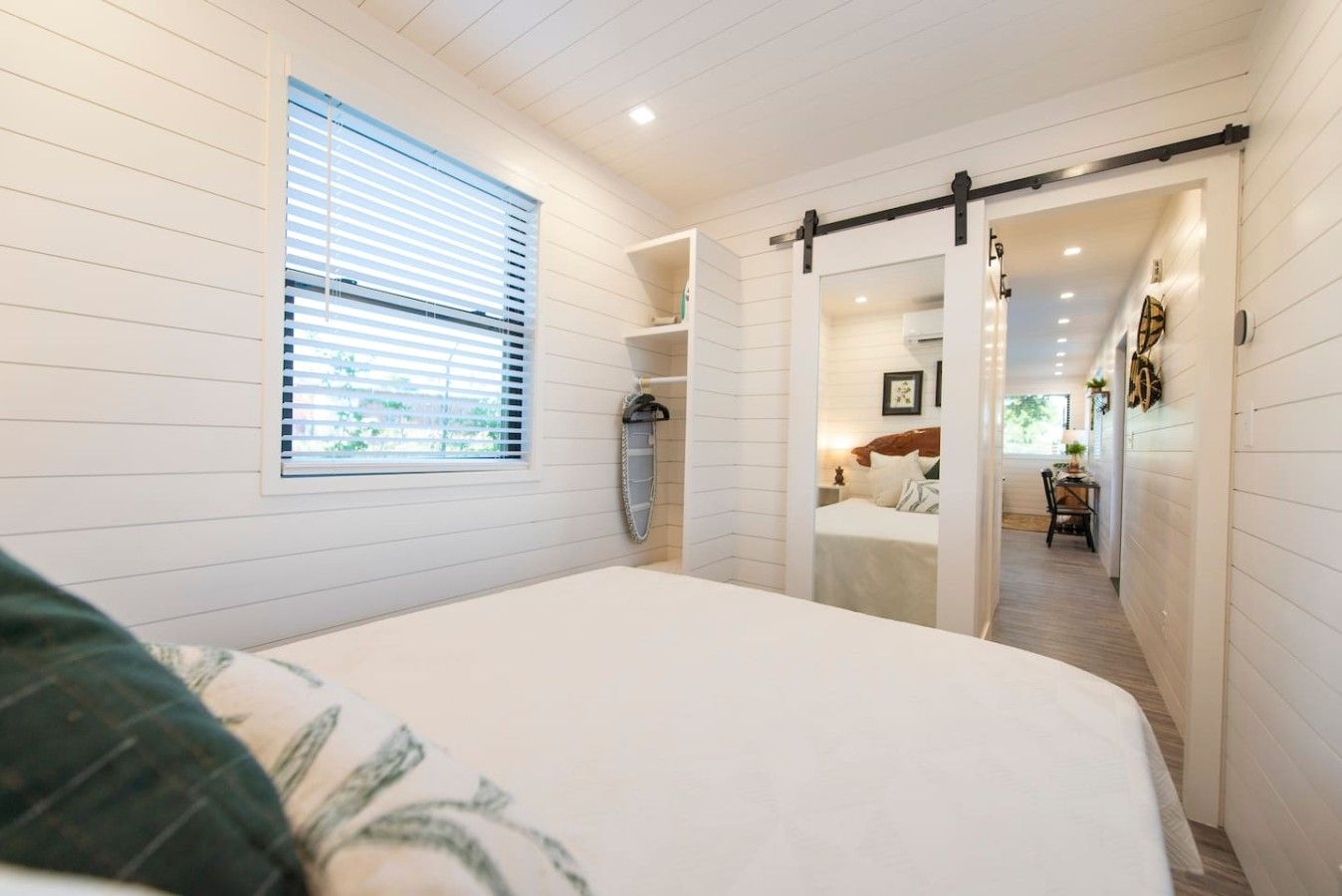 Une chambre à coucher avec un lit, une fenêtre avec des stores, une porte coulissante et un couloir menant à une salle de bain.