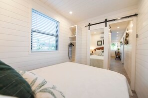 A bedroom with a bed, a window with blinds, a sliding door, and a hallway leading to a bathroom.