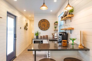 A modern kitchen with a central island, pendant lighting, and a large wall clock.