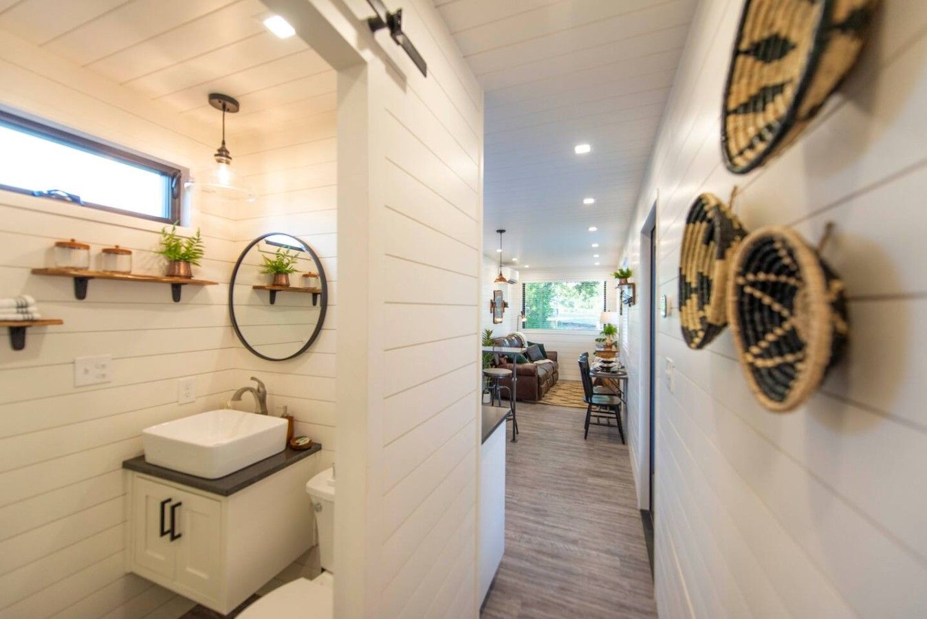 A modern bathroom with a white sink, mirror, and shelves with plants.