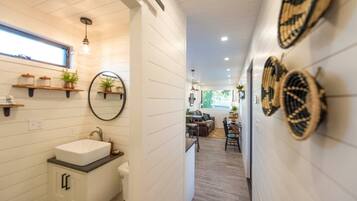 A modern bathroom with a white sink, mirror, and shelves with plants.