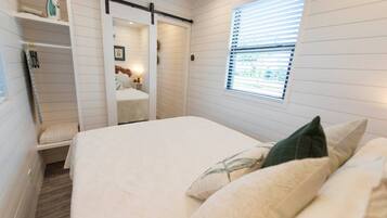 Een slaapkamer met een bed, een raam met jaloezieën, een schuifdeur en een plank met spullen.