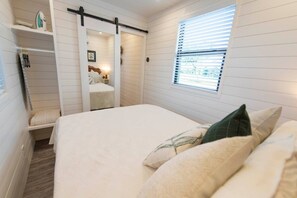A bedroom with a bed, a window with blinds, a sliding door, and a shelf with items. - "The Woods" Container | Pickleball | Rooftop Patio (Waco)