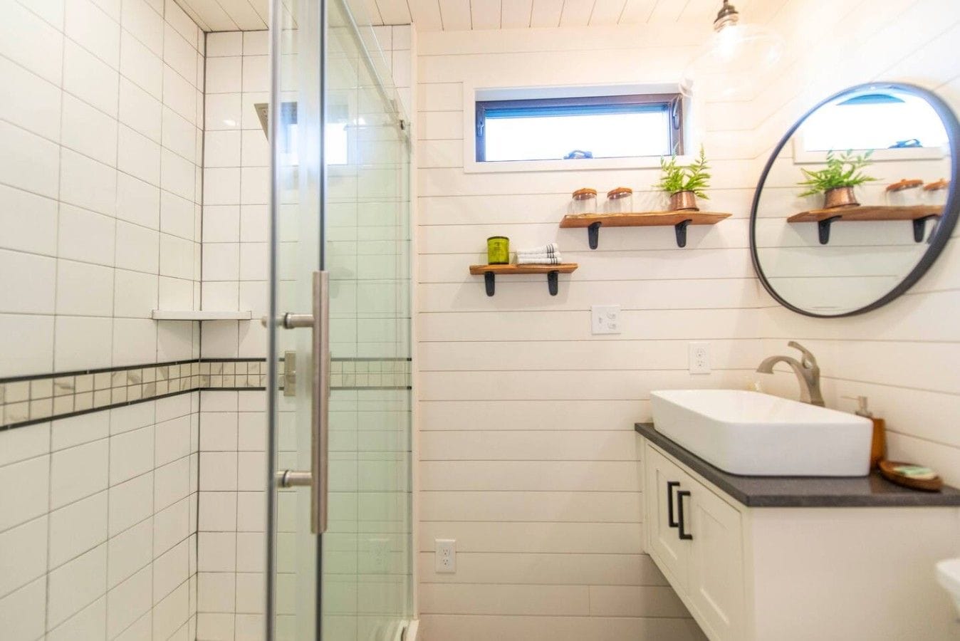 Une salle de bain avec une douche à parois de verre, un lavabo avec un miroir et des étagères ornées de plantes.