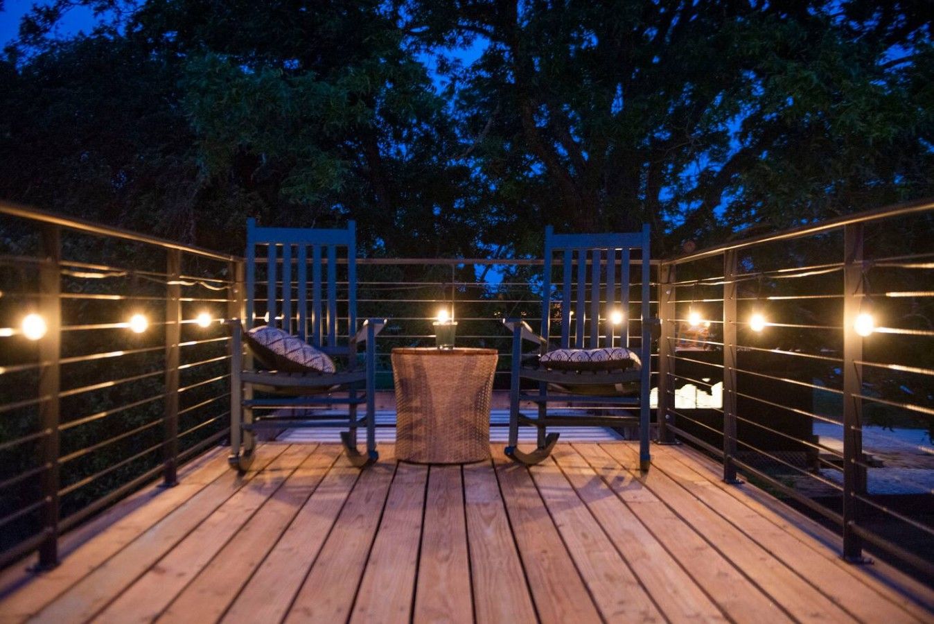Une terrasse extérieure avec un plancher en bois, deux chaises, une petite table ronde et des guirlandes lumineuses.