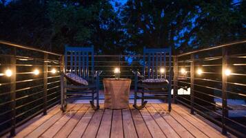 Une terrasse extérieure avec un plancher en bois, deux chaises, une petite table ronde et des guirlandes lumineuses.