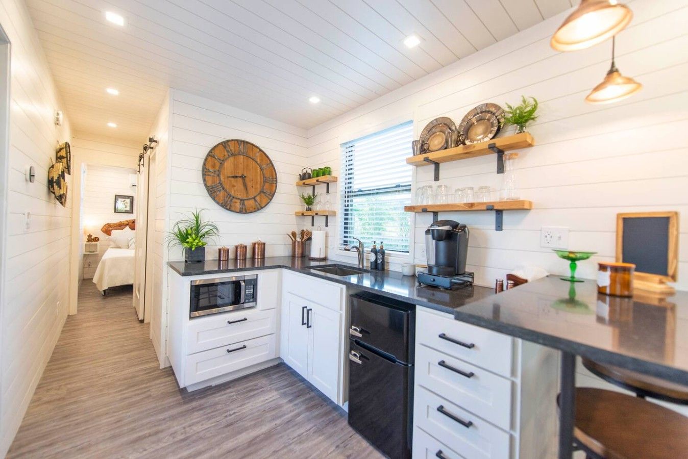 A modern kitchen with white cabinetry, a black countertop, and a wooden clock on the wall.