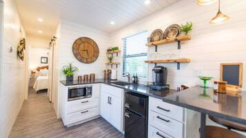 A modern kitchen with white cabinetry, a black countertop, and a wooden clock on the wall.