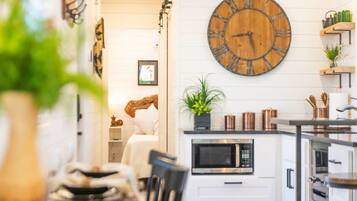 Une cuisine moderne avec une grande horloge en bois, des meubles blancs et un four à micro-ondes.