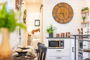 A modern kitchen with a large wooden clock, white cabinetry, and a microwave.