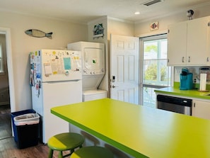 A kitchen with a green countertop, white cabinets, a refrigerator, a washing machine, and a trash bin.
