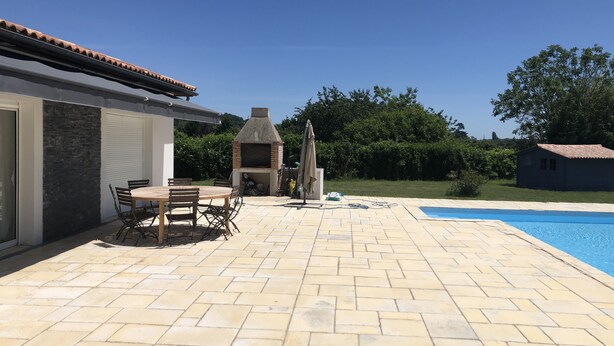Eine Terrasse mit Backsteinboden, einem Holztisch mit Stühlen, einem Grill und einem Swimmingpool.