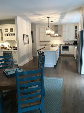 Cozinha moderna com armários brancos, uma ilha central e um espaço de jantar com cadeiras azuis.