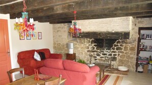 A cozy living room with a red sofa, wooden dining table, and chairs, a stone fireplace, and a bookshelf. - luxury gite for couples, no children. Peace, great views, large pool and spa. (Boisse, France)