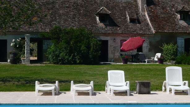 A pool area with white lounge chairs and a building with a red umbrella in the background. - luxury gite for couples, no children. Peace, great views, large pool and spa. (Boisse, France)