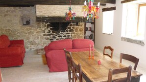 A cozy room with a stone fireplace, a wooden dining table with chairs, a red sofa, and a bookshelf. - luxury gite for couples, no children. Peace, great views, large pool and spa. (Boisse, France)