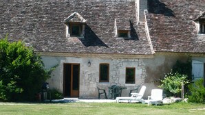 A rustic stone building with a tiled roof, a wooden door, and a small window. There are outdoor chairs and a table in front. - luxury gite for couples, no children. Peace, great views, large pool and spa. (Boisse, France)