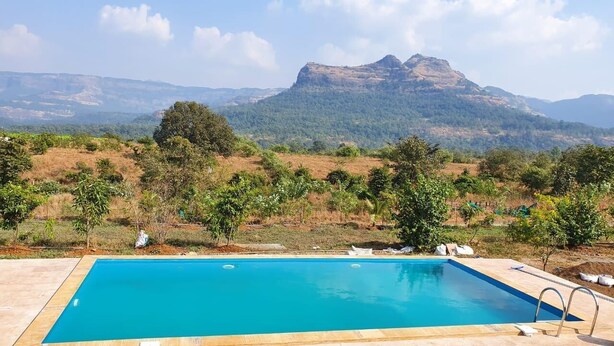 Una piscina rectangular con superficie de agua azul cristalina, rodeada por un solárium con baldosas. Al fondo, se ven colinas y una cadena montañosa bajo un cielo despejado.