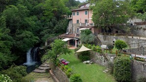 Un edificio de piedra con un balcón que da a un exuberante jardín y una cascada.