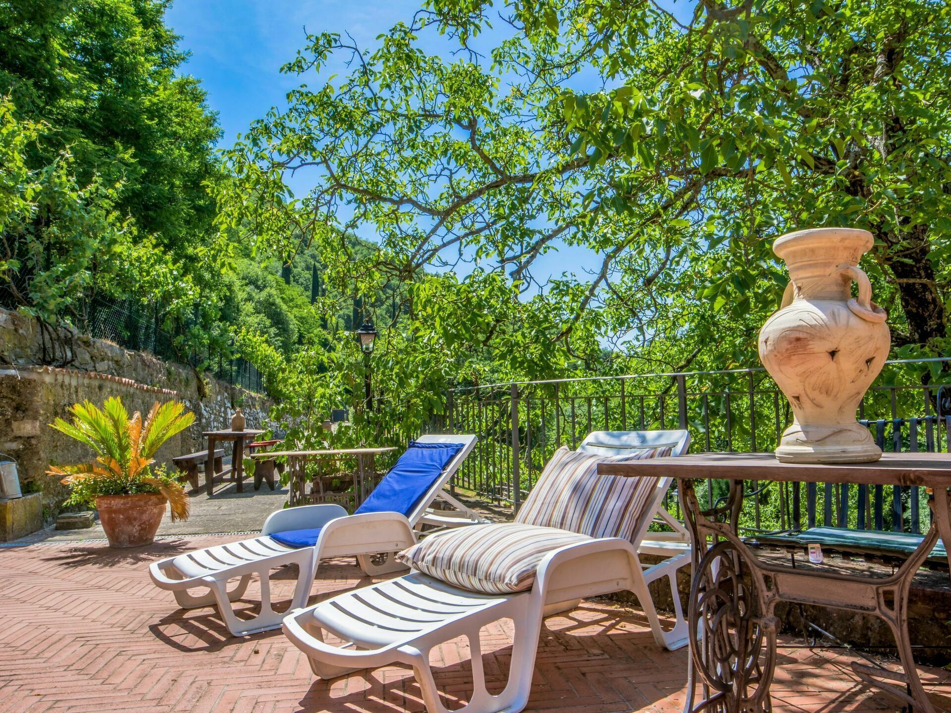 A patio area with white lounge chairs, a table with a vase, and a potted plant.